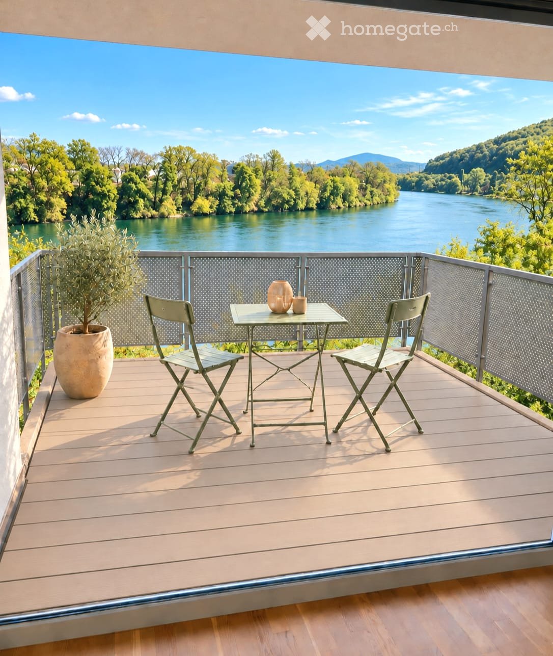 Balcony with wooden decking, metal railing, small table with two chairs, decorative vase, and potted plant, overlooking a river and green landscape.