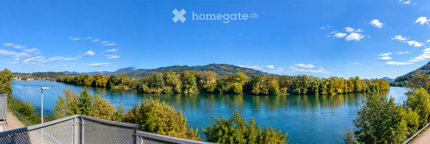 Balcony overlooking a river with surrounding trees and distant hills under a clear blue sky.