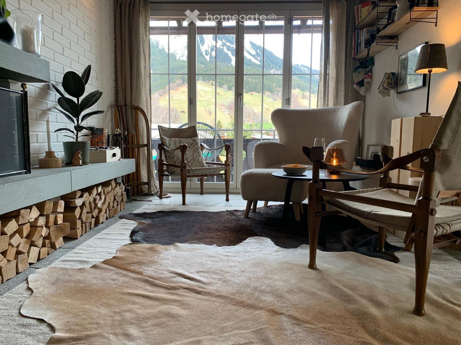 Cozy living room with a fireplace, large windows offering a scenic mountain view, a sofa, chairs, a coffee table, and a floor lamp.