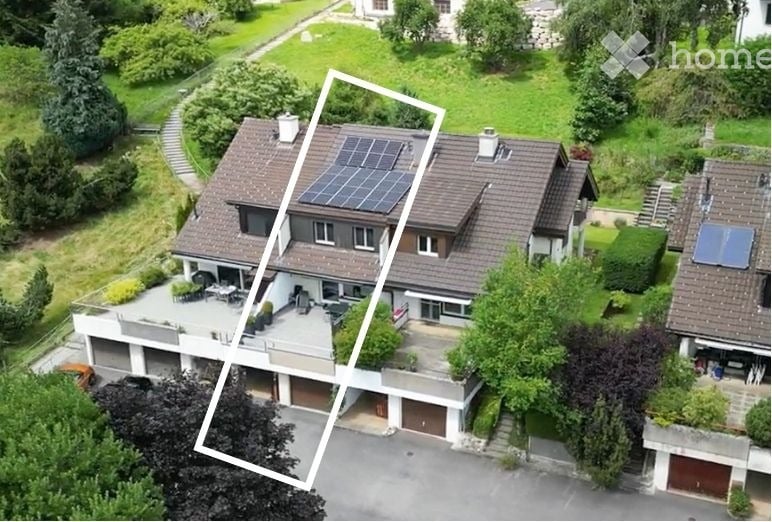 Aerial view of a two-story house with a garage, solar panels on the roof, and a well-maintained garden.