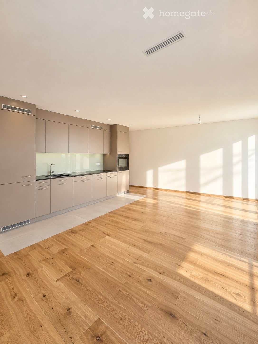 Modern kitchen with light wood flooring, grey cabinets, and a sleek sink area.