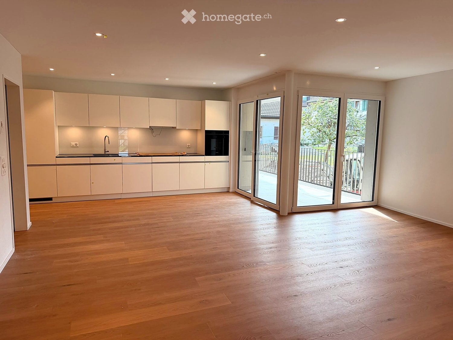 Empty kitchen with white cabinets, black countertops, and wooden flooring. Large sliding glass doors lead to an outdoor area.