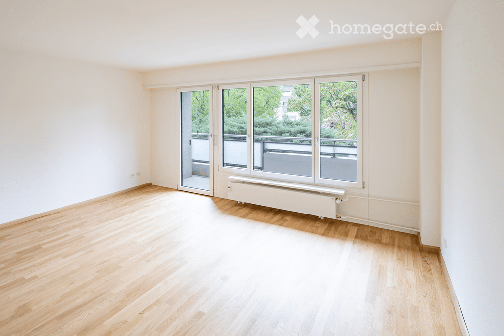 Empty room with wooden flooring, large windows, and a sliding door leading to a balcony.