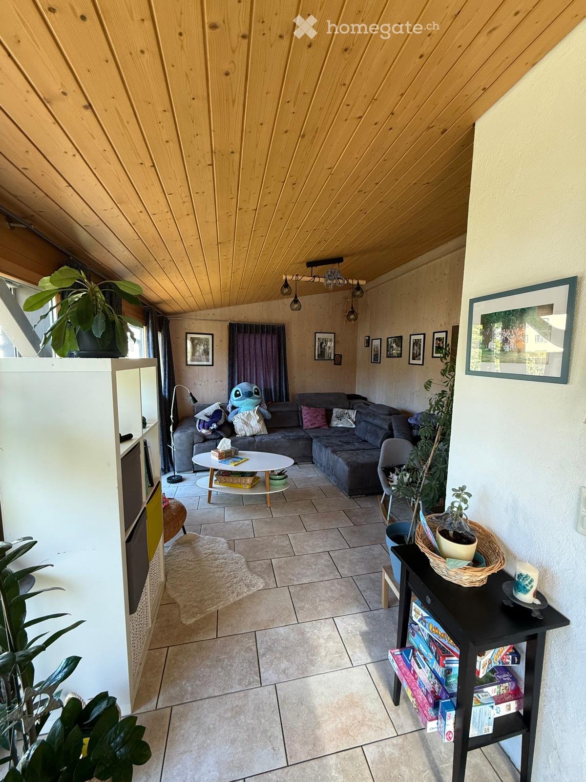 Living room with a grey sectional sofa, coffee table, small round table, and various decorative items including plants and picture frames.