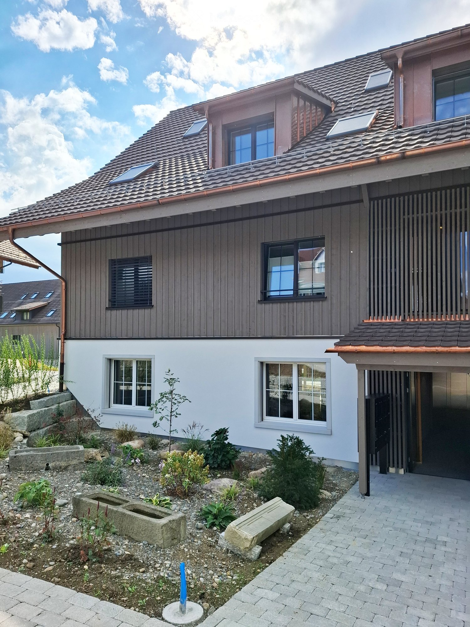 Two-story house with a tiled roof, solar panels, and a landscaped garden with stone planters and small plants.