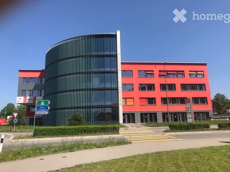 Modern office building with red and green facades, glass windows, and a curved section.