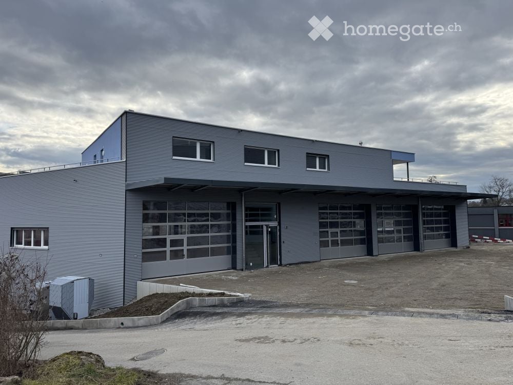 Modern industrial-style building with large garage doors, grey metal facade, and multiple windows.
