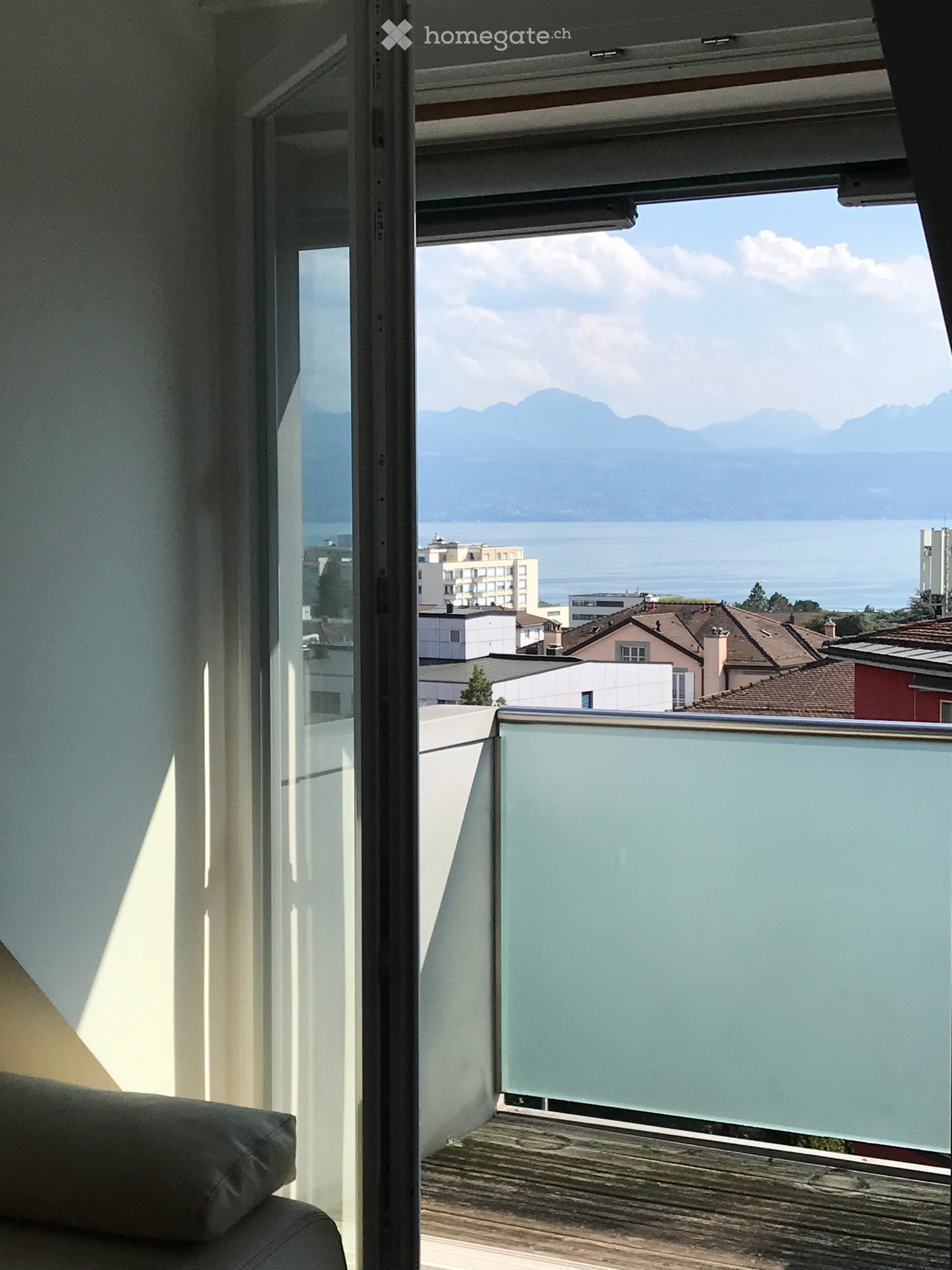 Balcony with wooden decking, glass railing, and scenic view of mountains and lake.