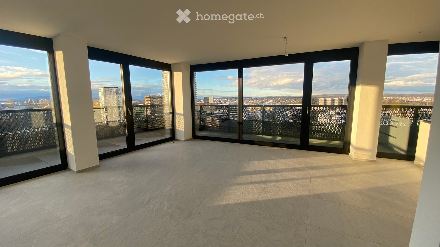 Empty room with large sliding glass doors leading to a balcony, tiled floor, and cityscape view.