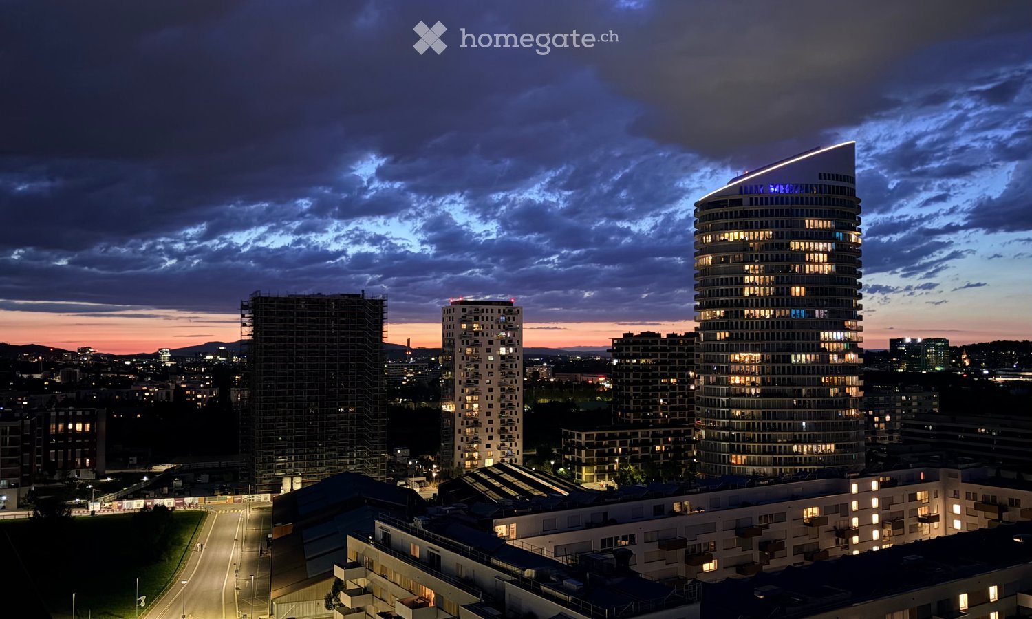 A cityscape at dusk with multiple high-rise buildings, some under construction, and illuminated windows.