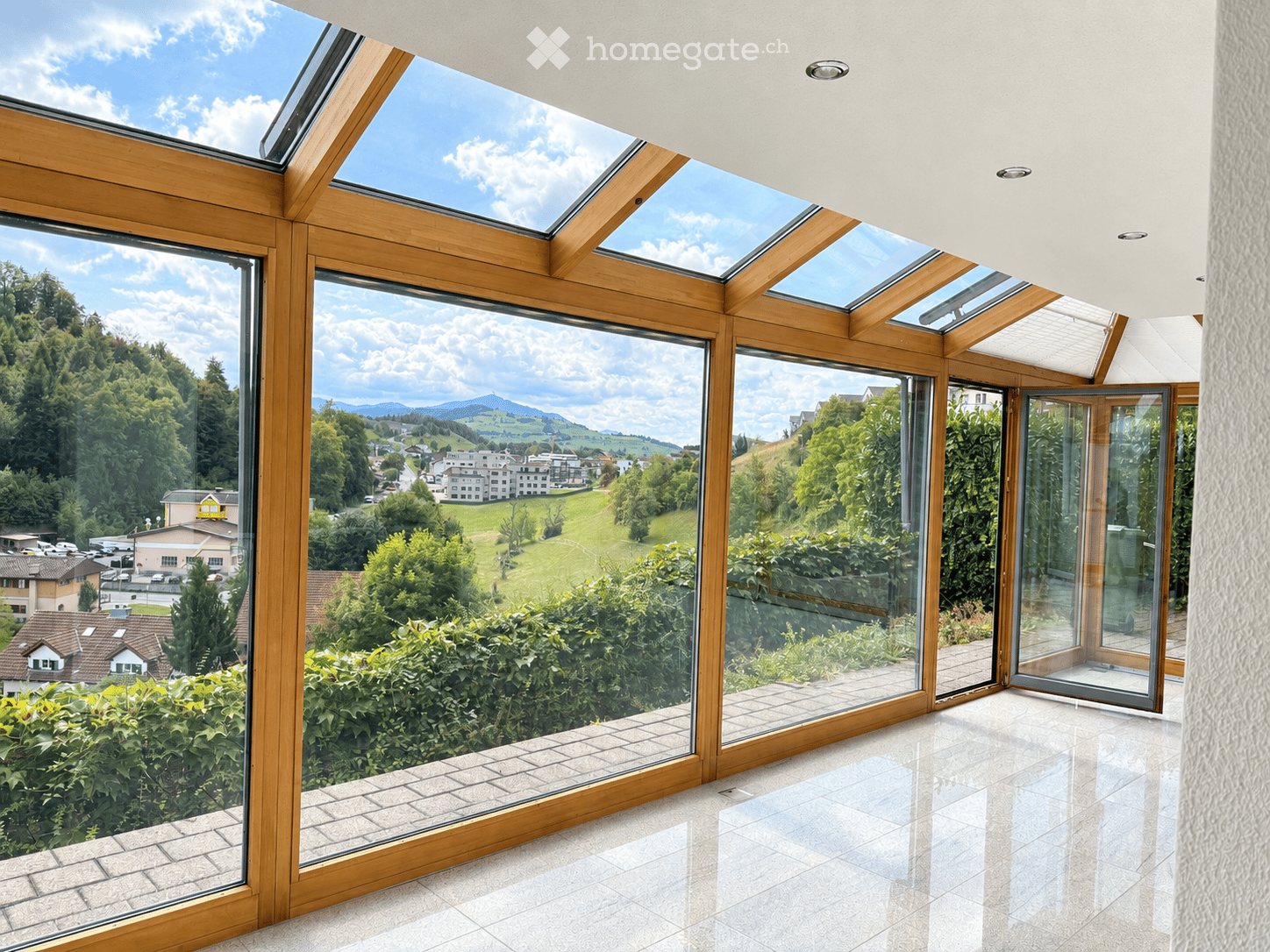 Bright, unfurnished room with large windows and skylights offering a scenic view of a green landscape and distant mountains.