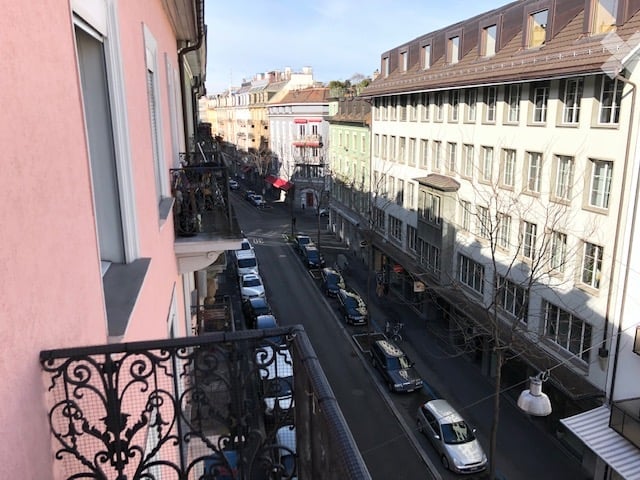 Balcony overlooking a city street with parked cars and buildings on both sides.