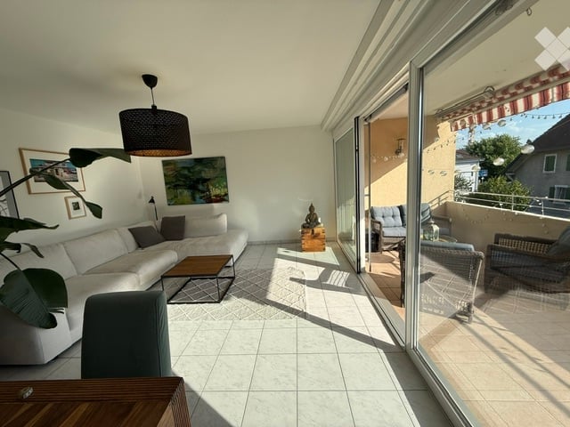 Bright living room with large sliding glass doors opening to a balcony, white sofa, coffee table, floor lamp, and artwork on the walls.