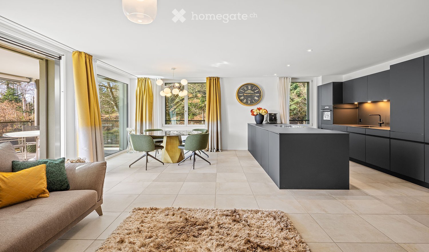 Open-plan living and dining area with a modern kitchen, featuring a sofa, dining table, chairs, kitchen island, and cabinets.