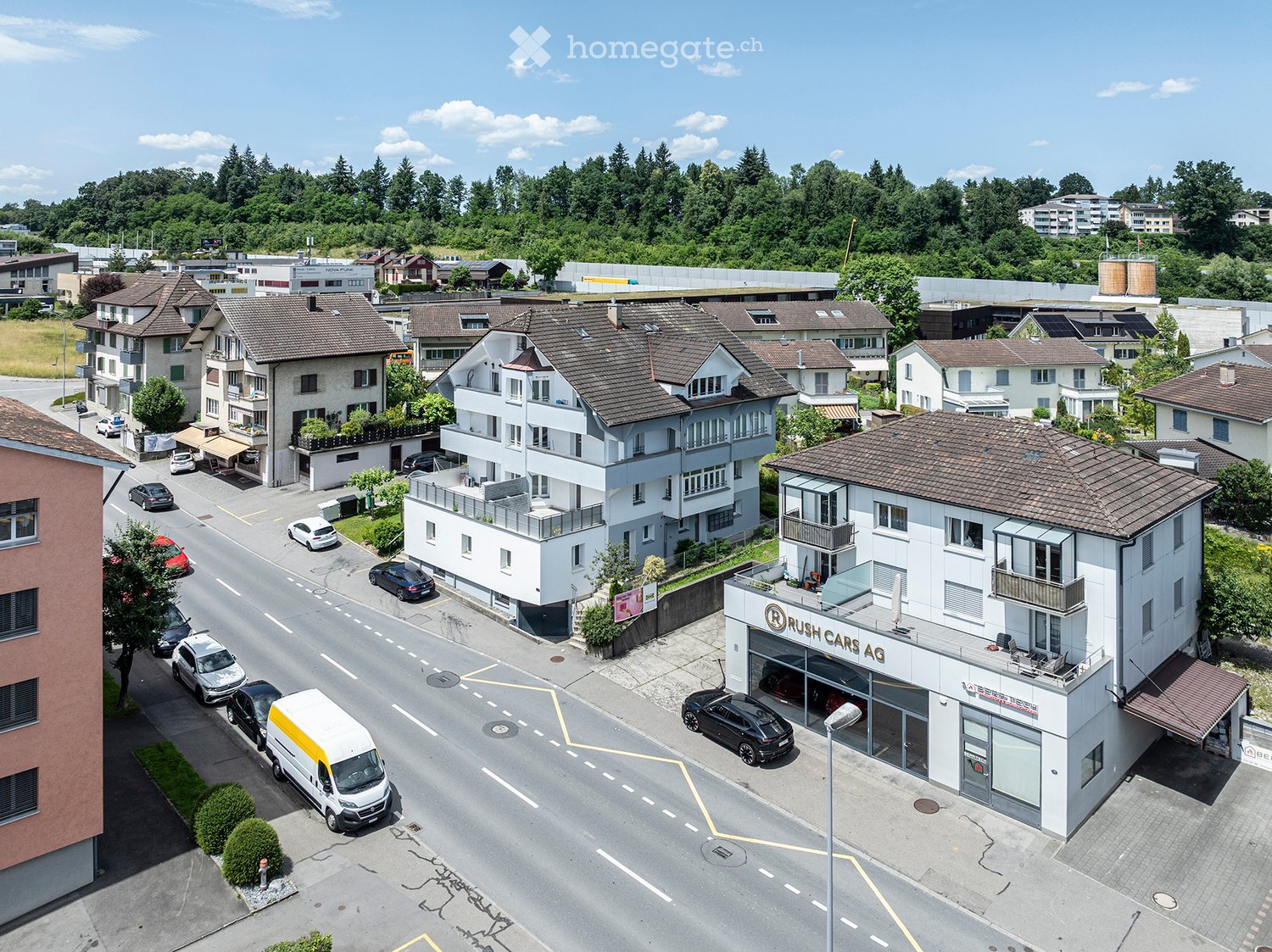Aerial view of a residential area with multiple multi-story houses, a car dealership, and surrounding greenery.