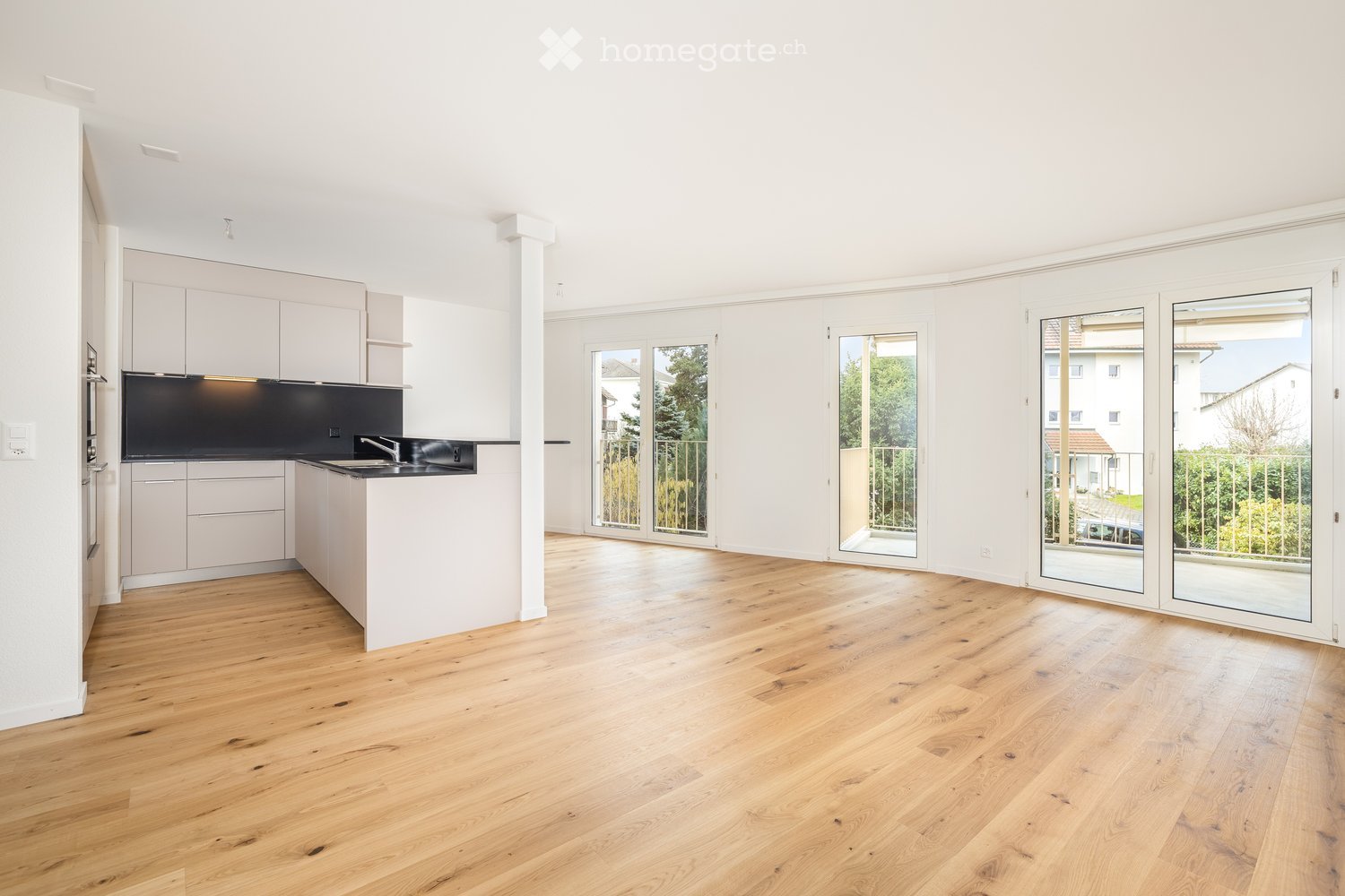 Empty kitchen with light wooden flooring, white cabinets, and large sliding glass doors leading to a balcony.