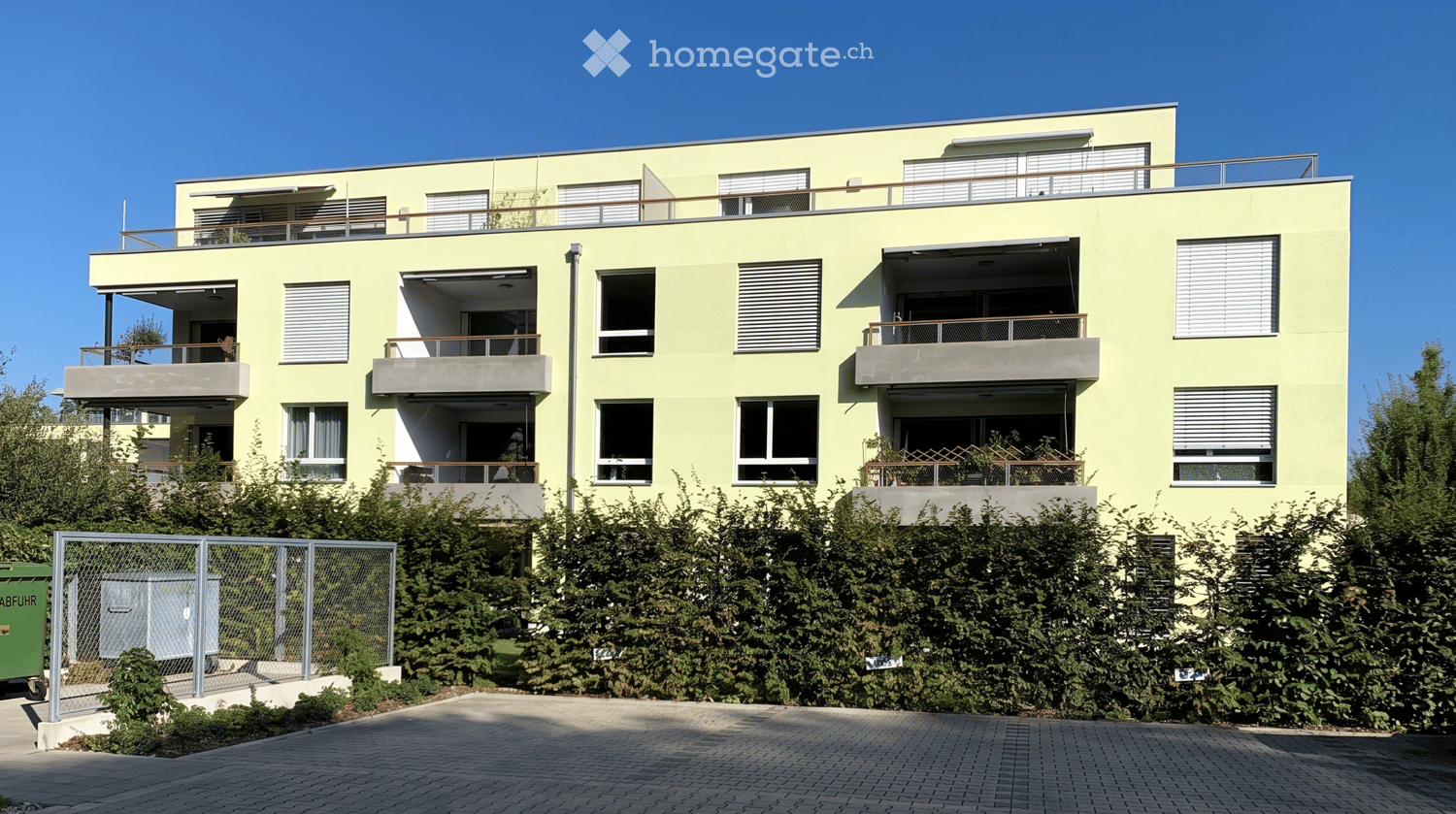 Modern three-story residential building with light yellow facade, multiple balconies, and large windows.