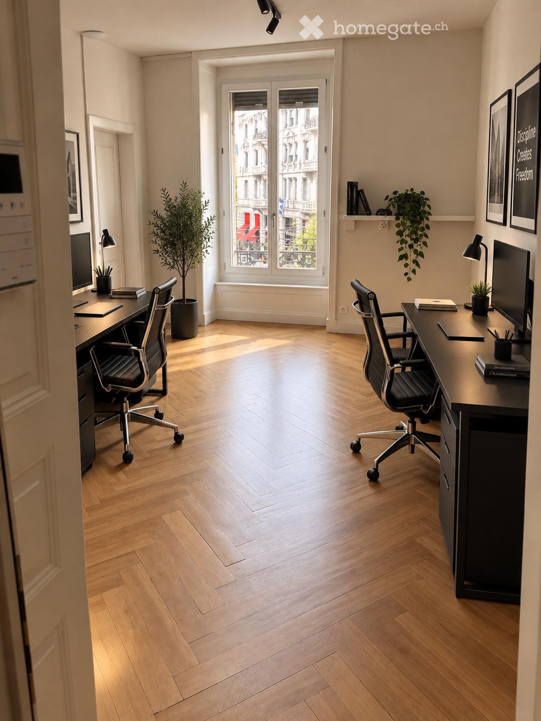 Modern office space with wooden herringbone flooring, two desks with chairs, computer screens, lamps, potted plants, and shelves with books and decorative items.