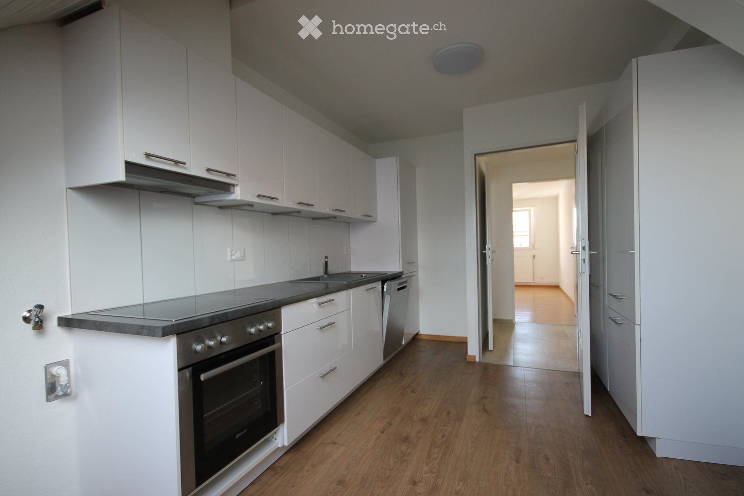 Modern kitchen with white cabinets, stainless steel appliances, and wooden flooring.