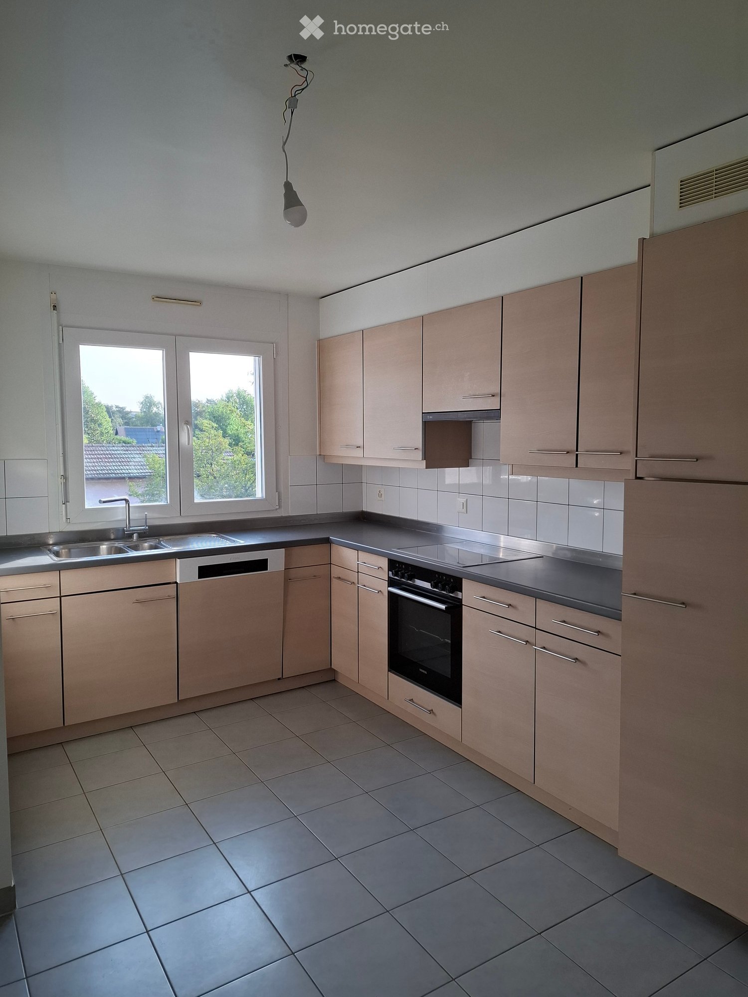 Modern kitchen with light wood cabinets, stainless steel appliances, tiled floor, and large windows.