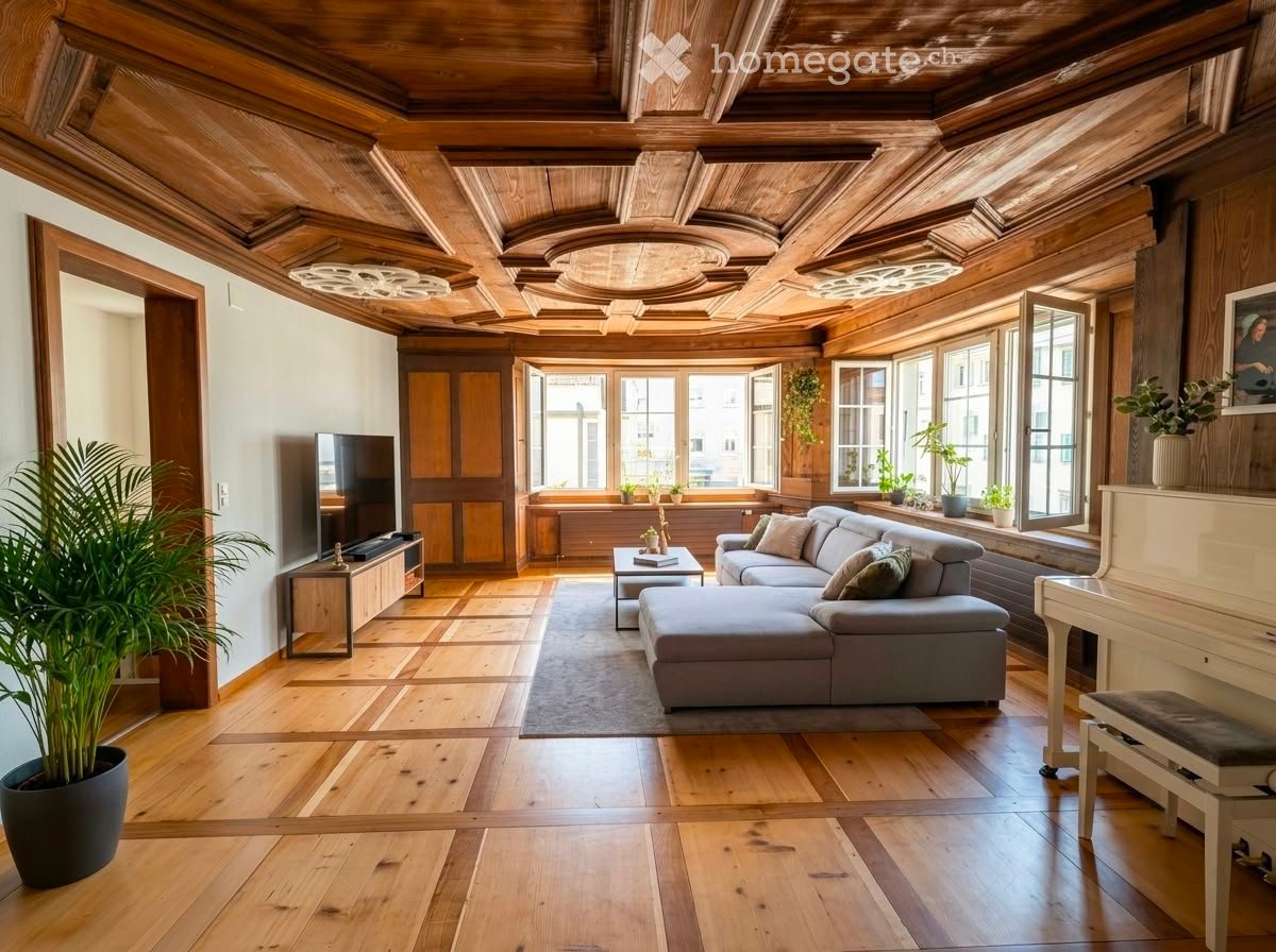 Living room with wooden ceiling, large windows, grey sectional sofa, coffee table, piano, and potted plants.