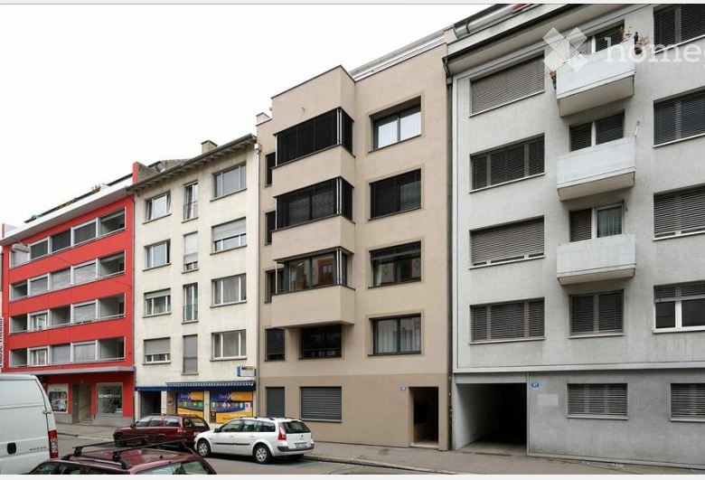 Multi-story residential building with beige and red facades, multiple windows, balconies, and a visible garage entrance.
