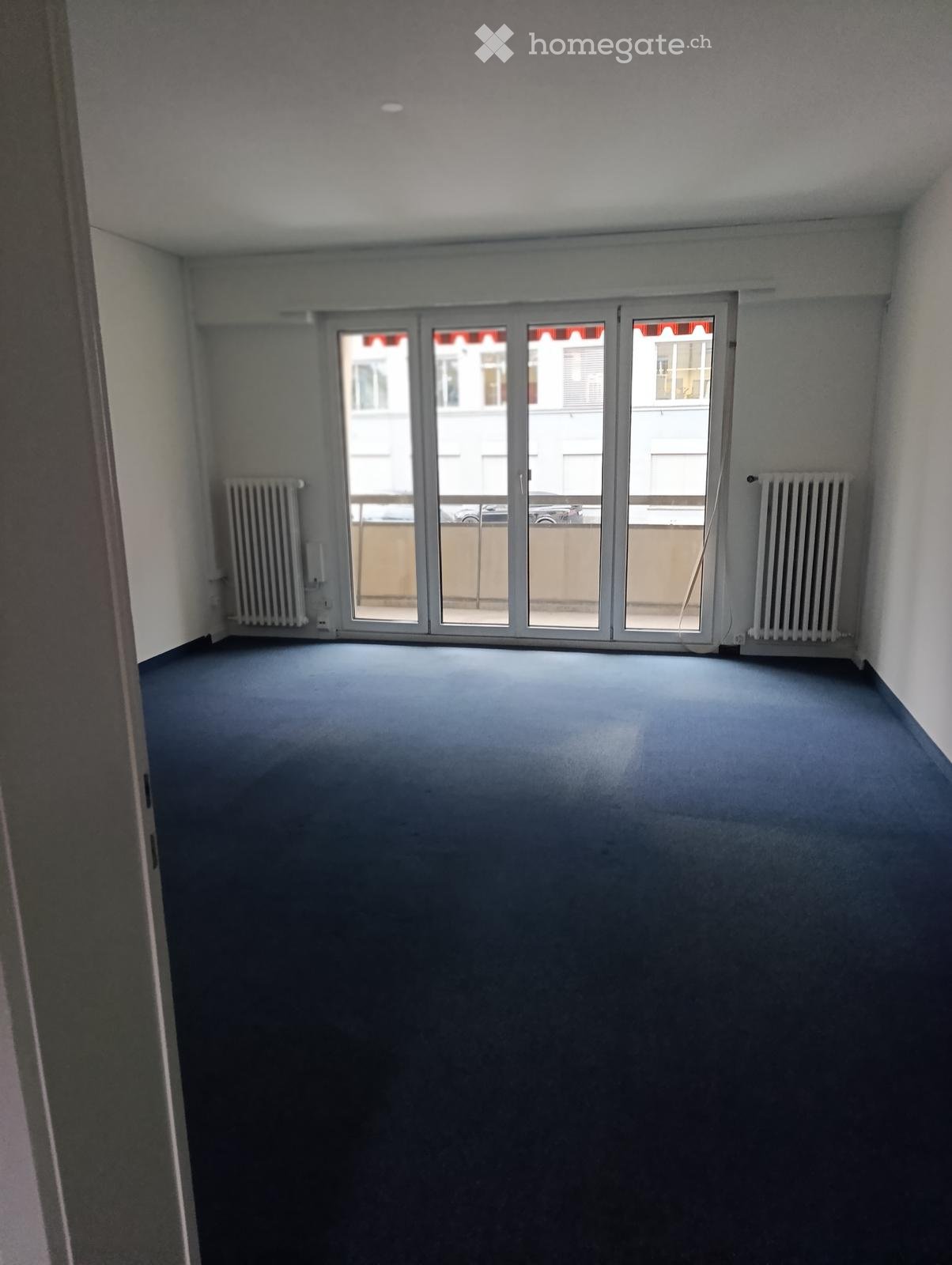 Empty room with blue carpet, white walls, and large sliding glass doors leading to a balcony area.