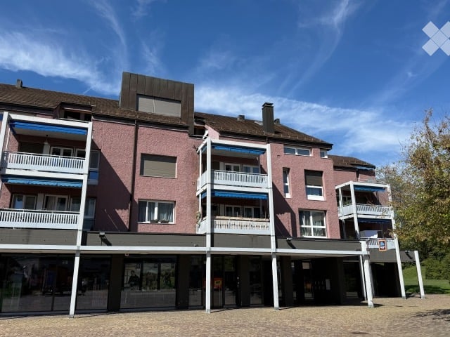 Multi-story residential building with pink brick facade, multiple balconies, and a covered ground floor entrance area.