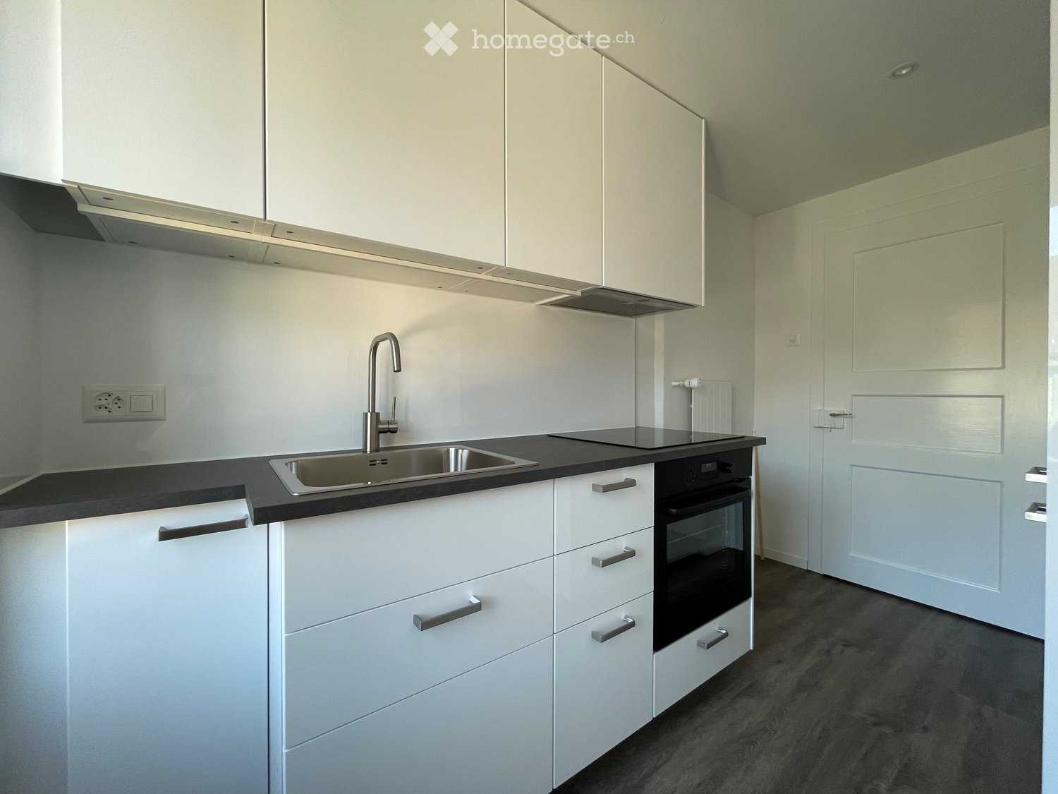 Modern kitchen with white cabinets, black countertop, stainless steel sink, and built-in oven.