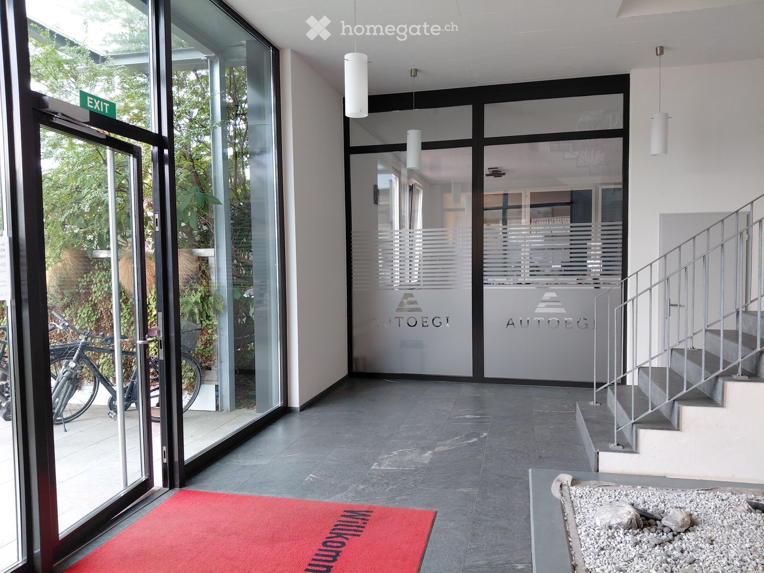 Modern hallway with glass doors, staircase, and a red welcome mat.