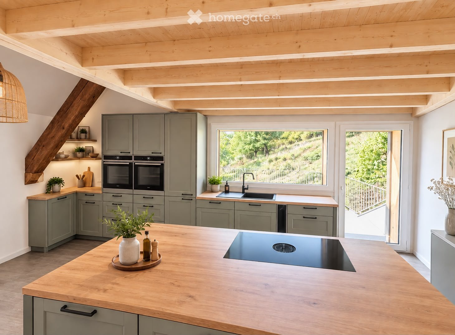 Modern kitchen with grey cabinets, wooden countertops, double oven, induction cooktop, and large windows overlooking a garden.