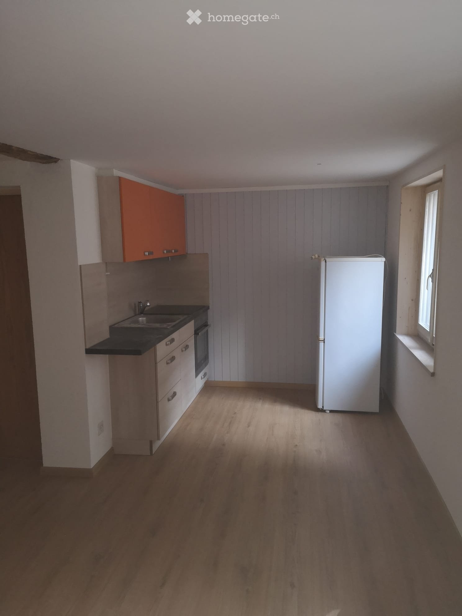 Empty kitchen with wooden flooring, white refrigerator, sink, oven, and cabinets.