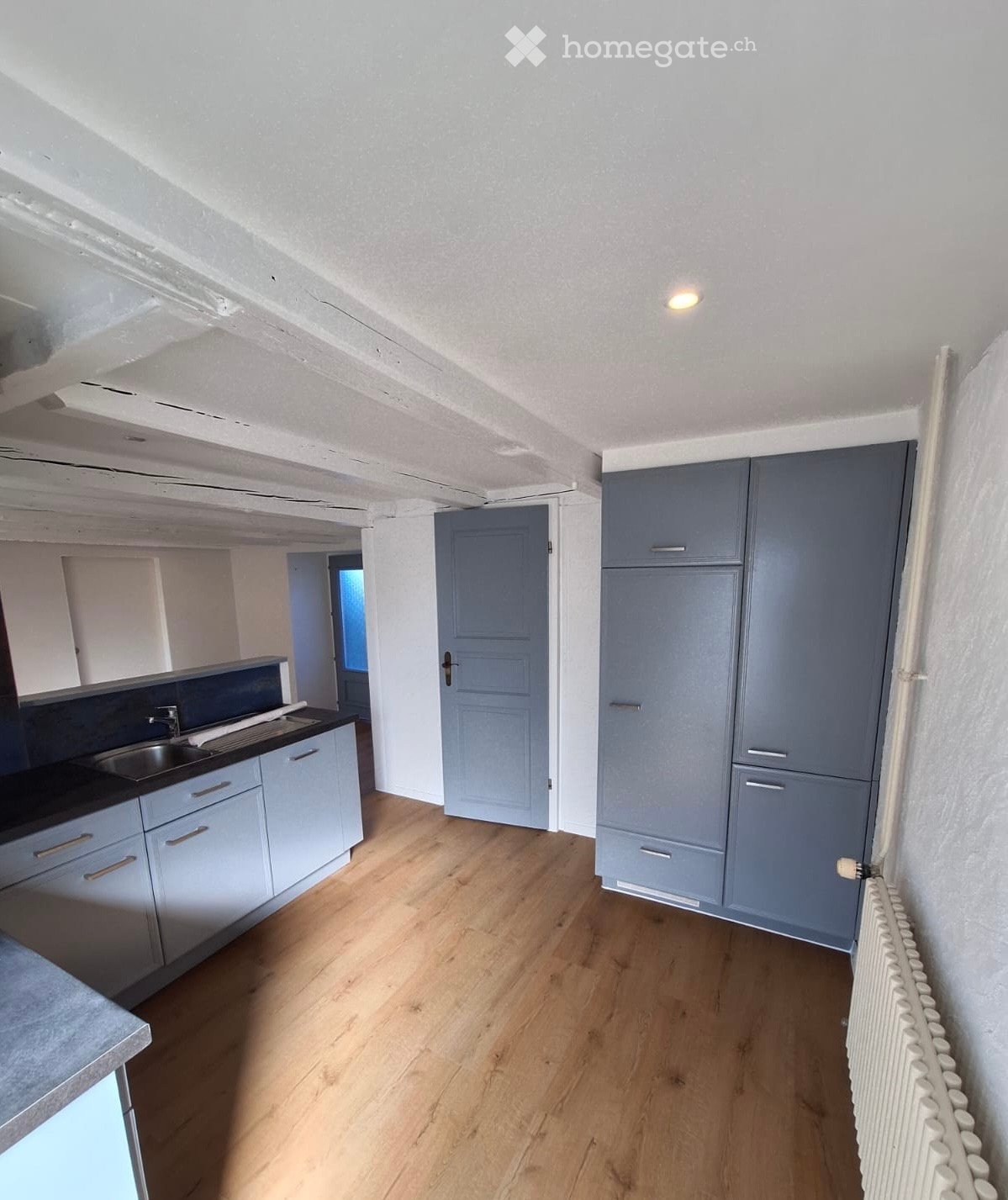 Empty kitchen with light blue cabinets, wooden flooring, and a sink area.