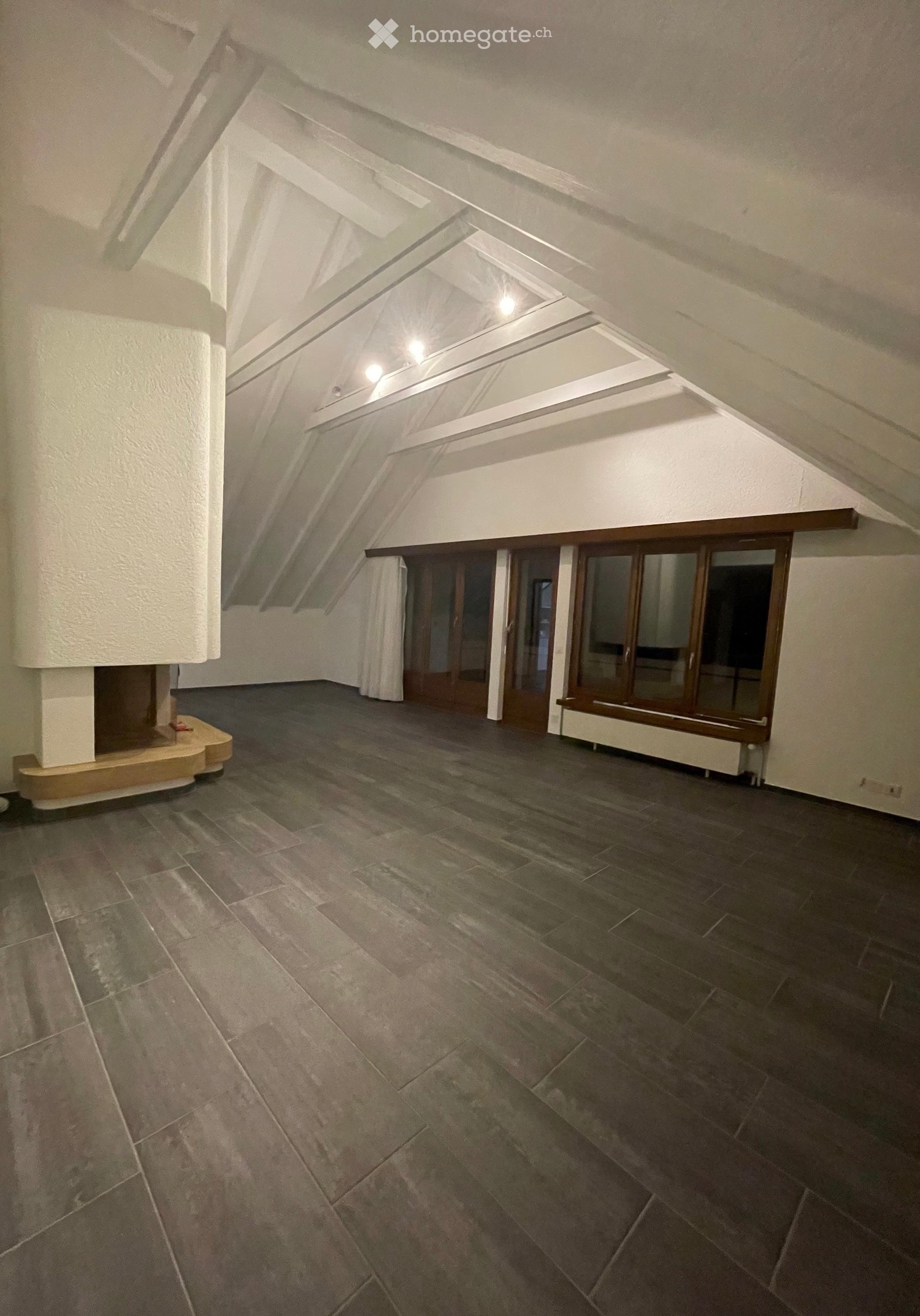 Empty attic space with exposed wooden beams, skylights, and dark tiled flooring. No furniture or equipment visible.