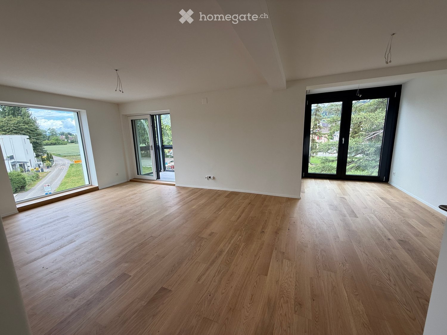 Empty room with wooden flooring, large windows, and sliding doors leading to an outdoor area.