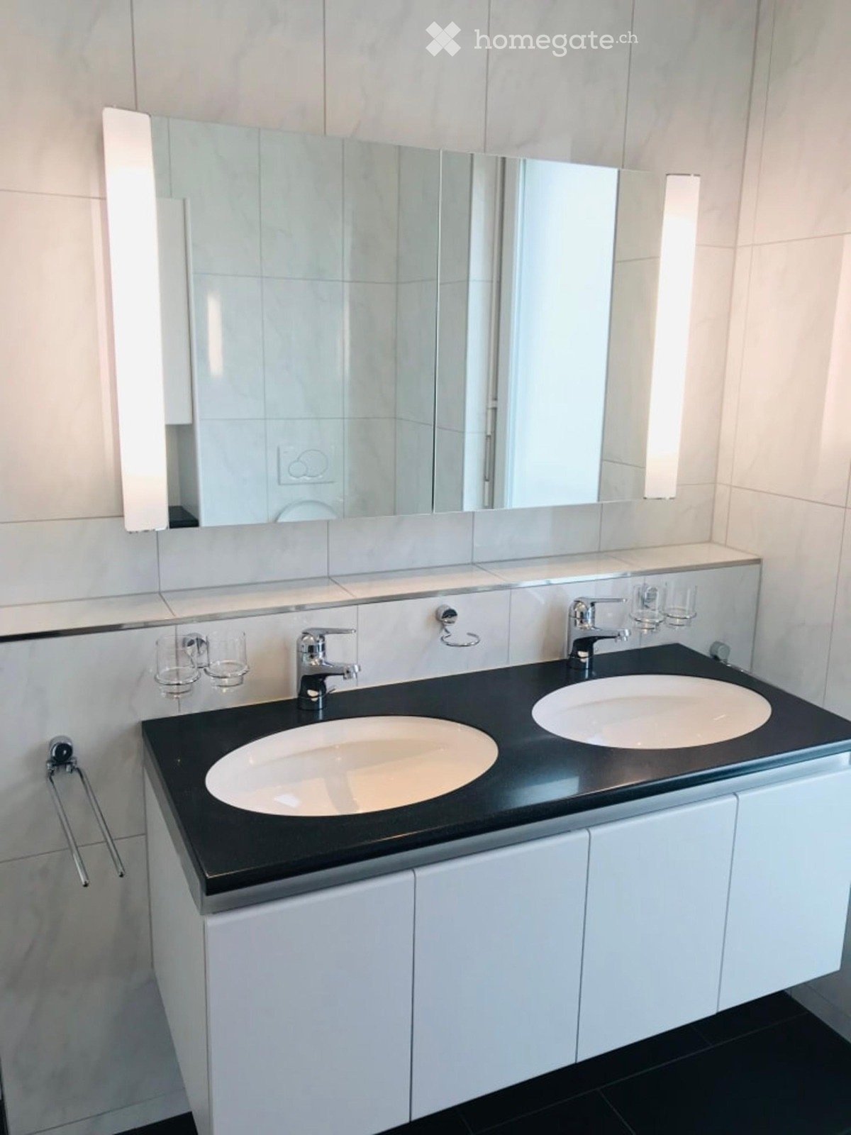 Modern bathroom with double sink vanity, black countertop, white cabinets, and large mirror with built-in lighting.