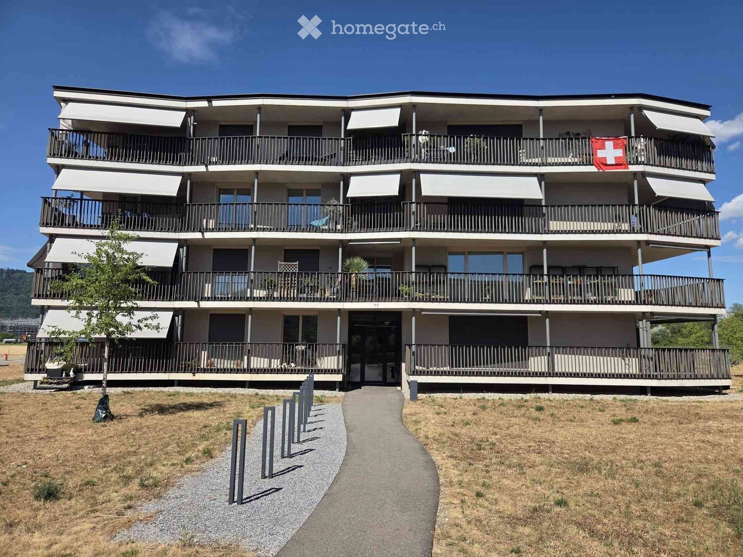 Modern multi-story building with balconies, large windows, and a Swiss flag displayed on the upper level.