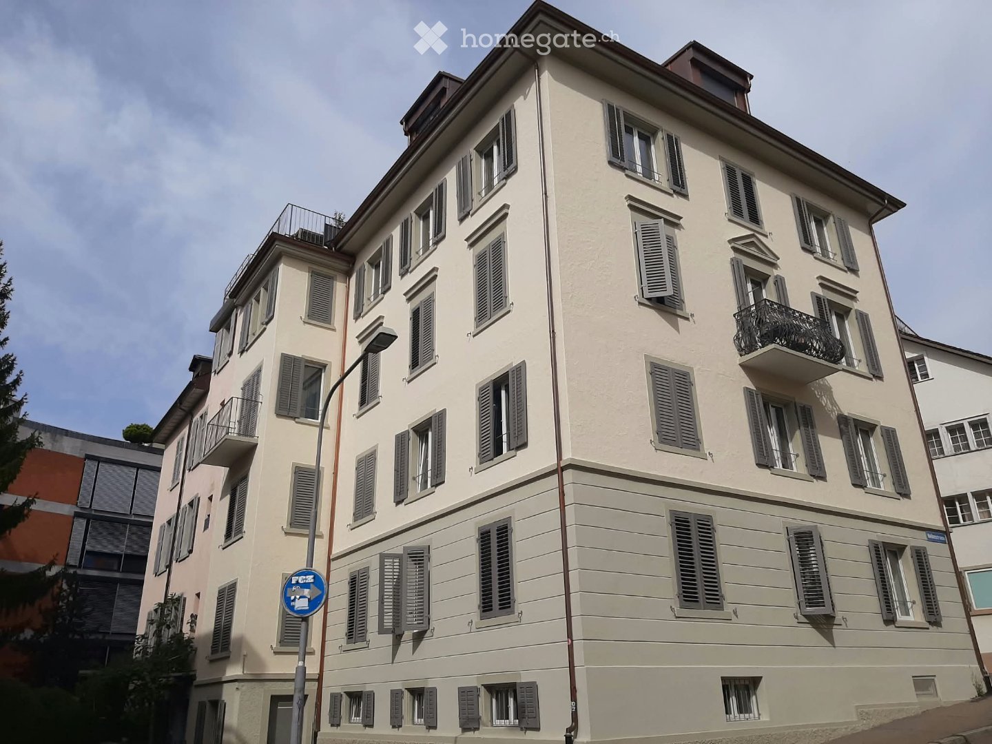 Four-story residential building with light beige facade, multiple windows with shutters, and balconies on upper floors.