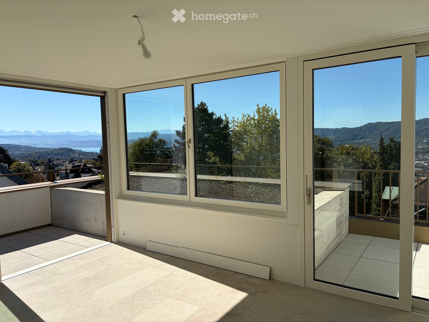 Bright, spacious balcony with large glass doors, tiled floor, and expansive scenic views of mountains and cityscape.