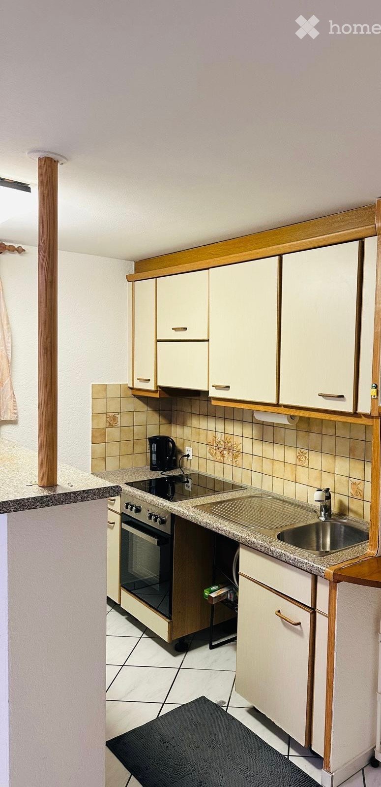 A compact kitchen with white cabinets, a granite countertop, a sink, an oven, and a coffee maker. The walls are tiled, and the floor is tiled as well.