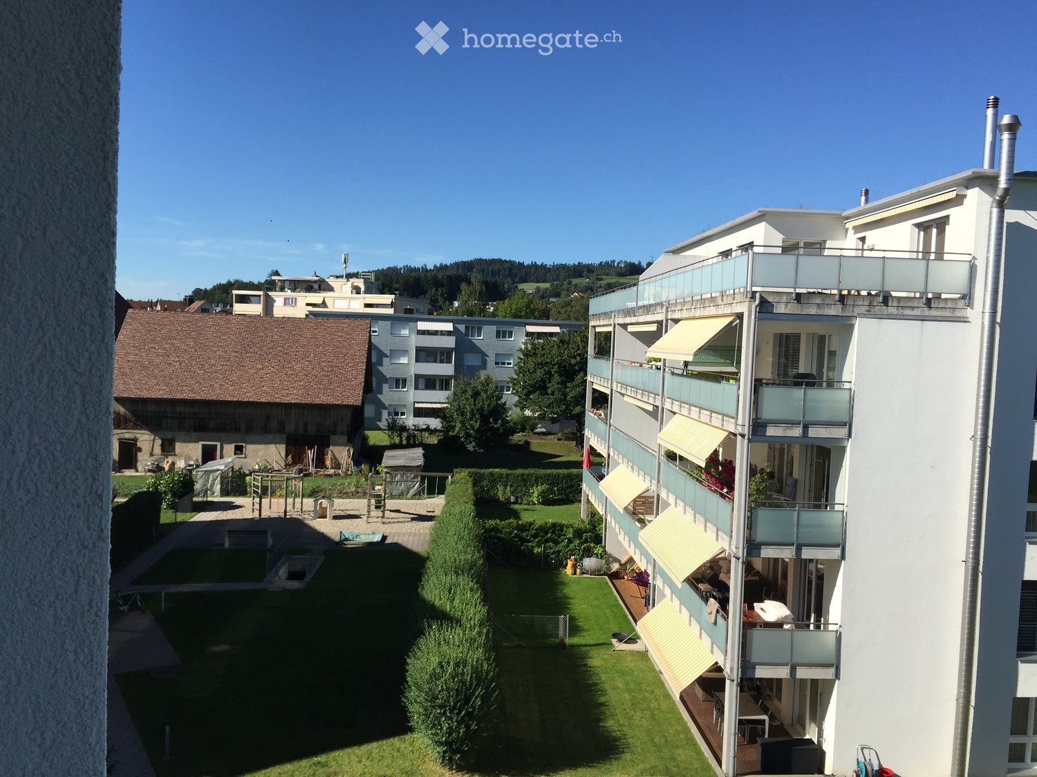 Multi-story residential building with balconies, awnings, and a well-maintained garden area with a swimming pool and playground.