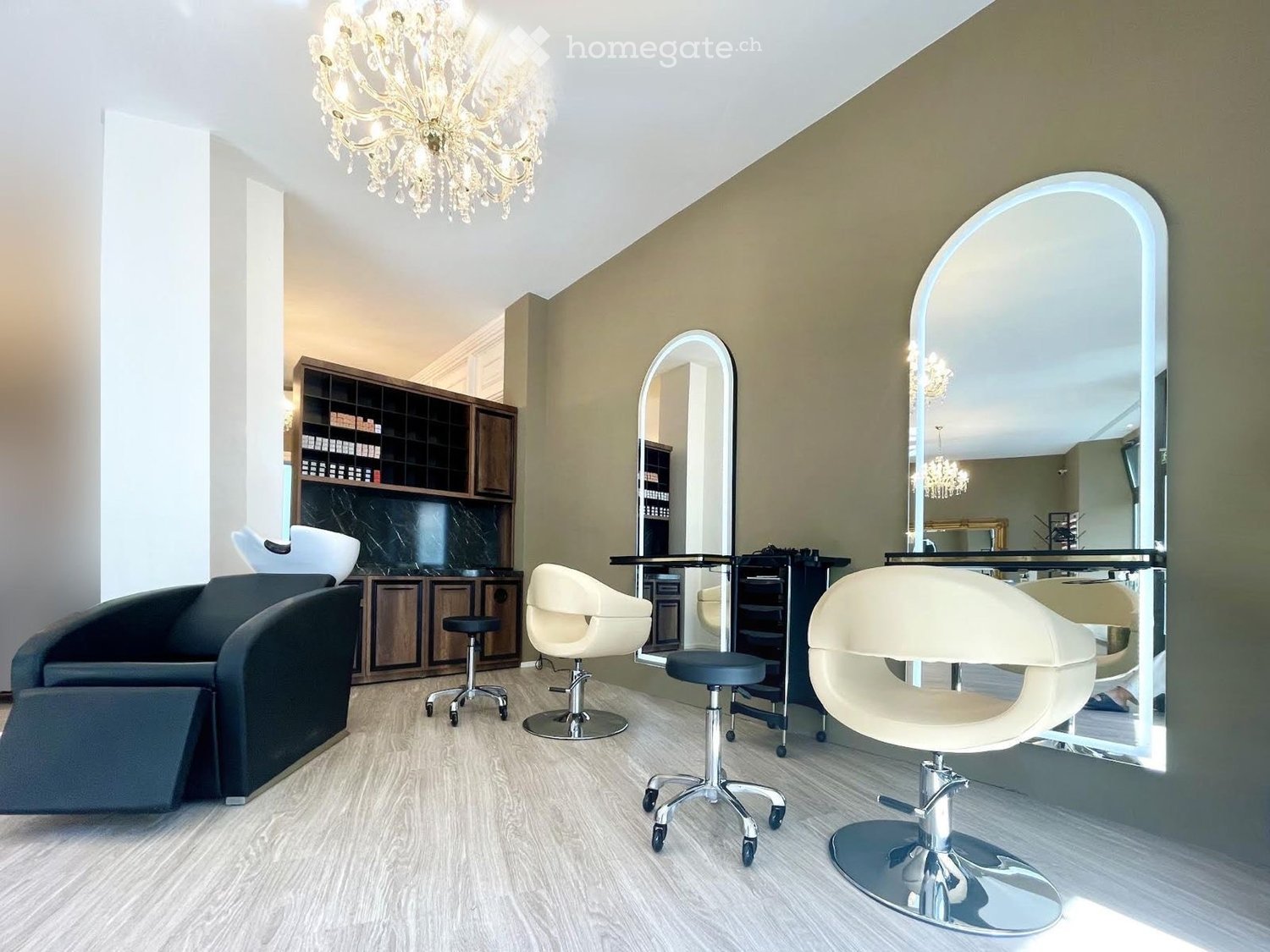 Modern salon with light-colored flooring, multiple salon chairs, mirrors, and a wooden cabinet with shelves.