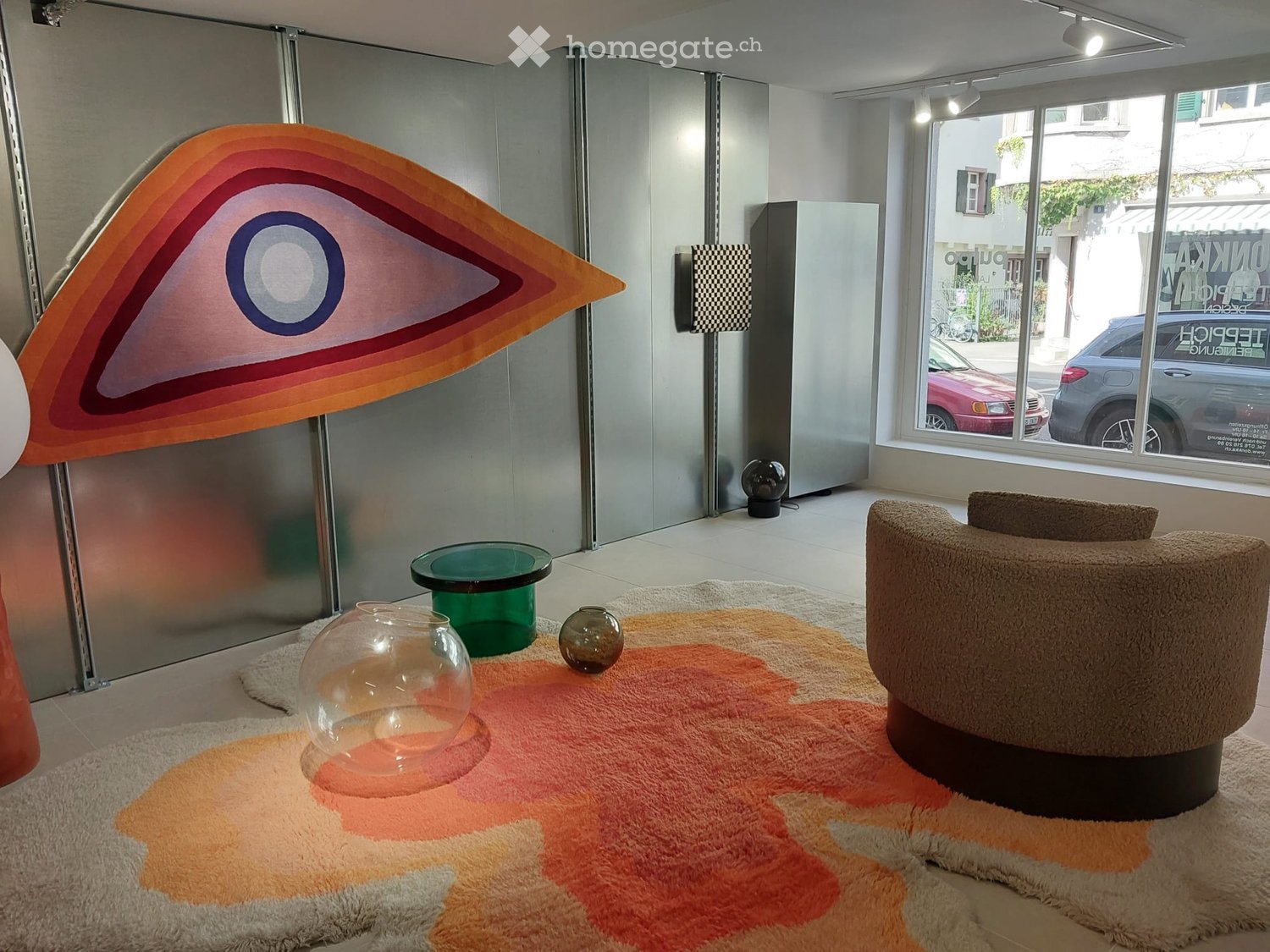 Modern living room with a round sofa, glass table, decorative vases, and a colorful rug.