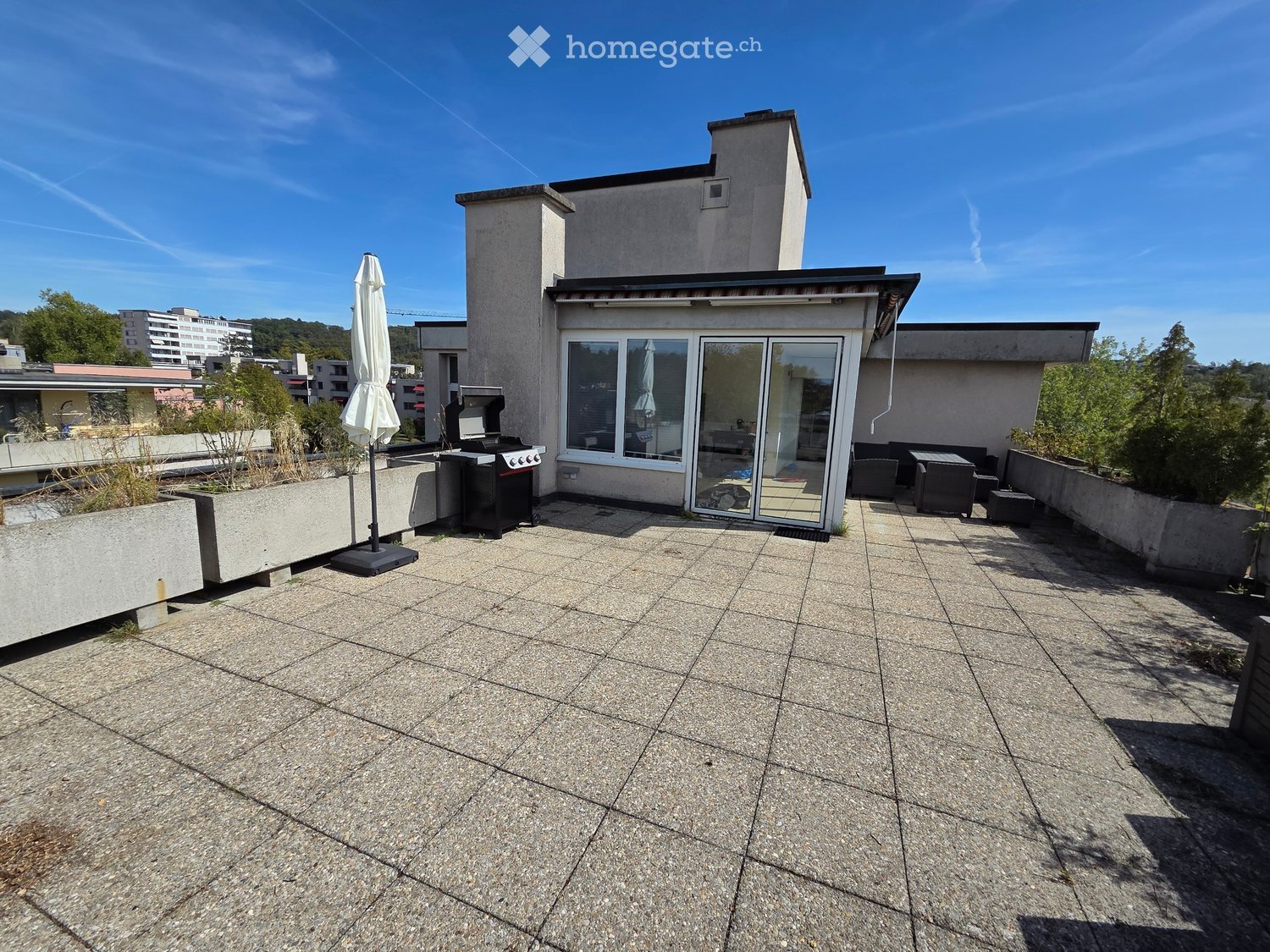 Roof terrace with tiled flooring, umbrella, grill, seating area, and surrounding greenery.