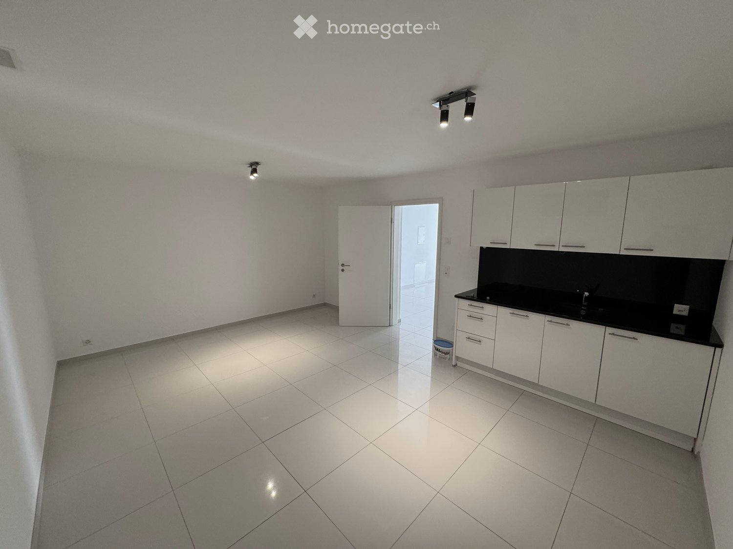 Empty kitchen with white tiled floor, white cabinets, and a black countertop. No appliances or furniture are present.