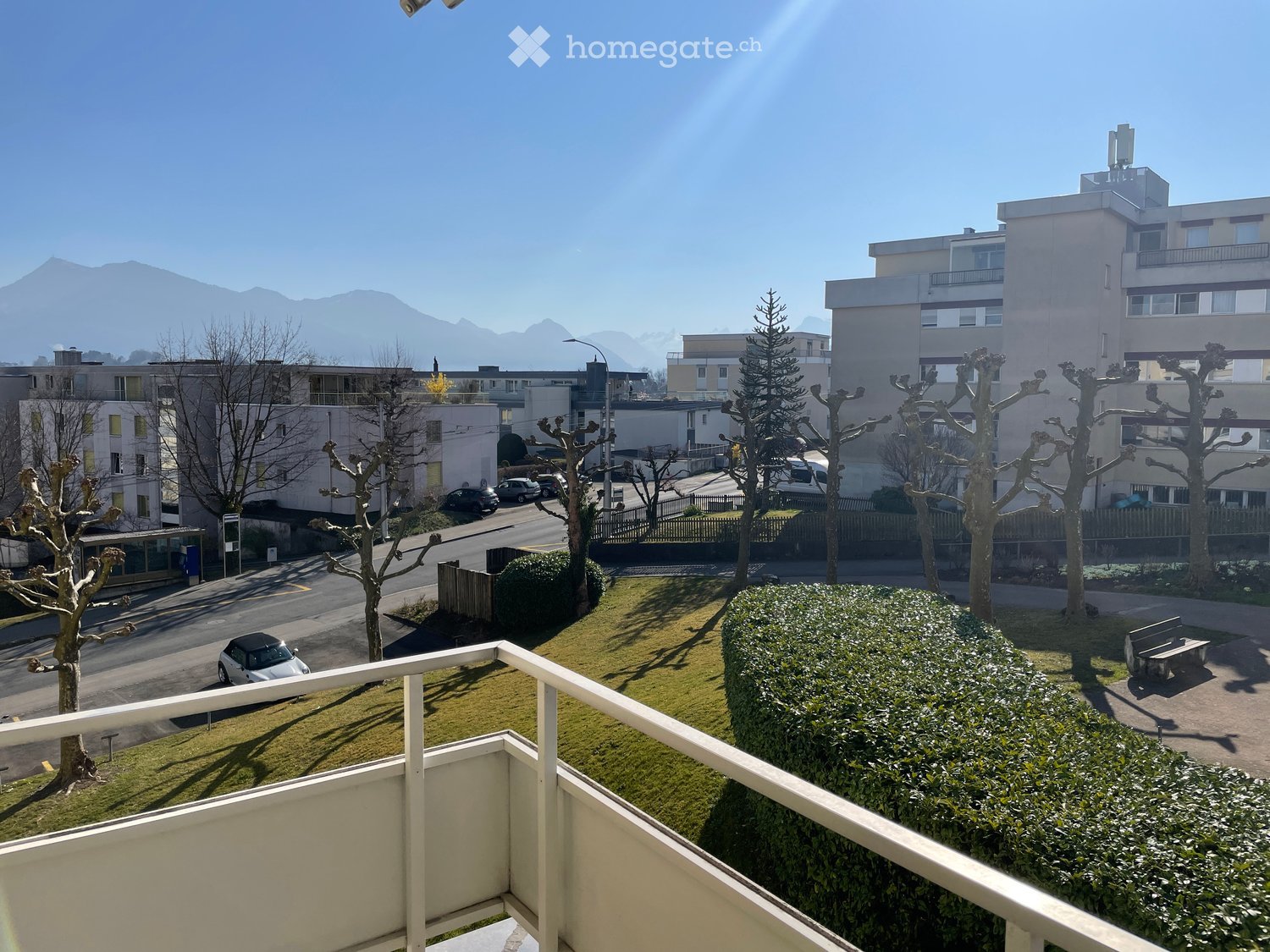 Balcony overlooking a residential area with trees, a bench, and distant mountains.