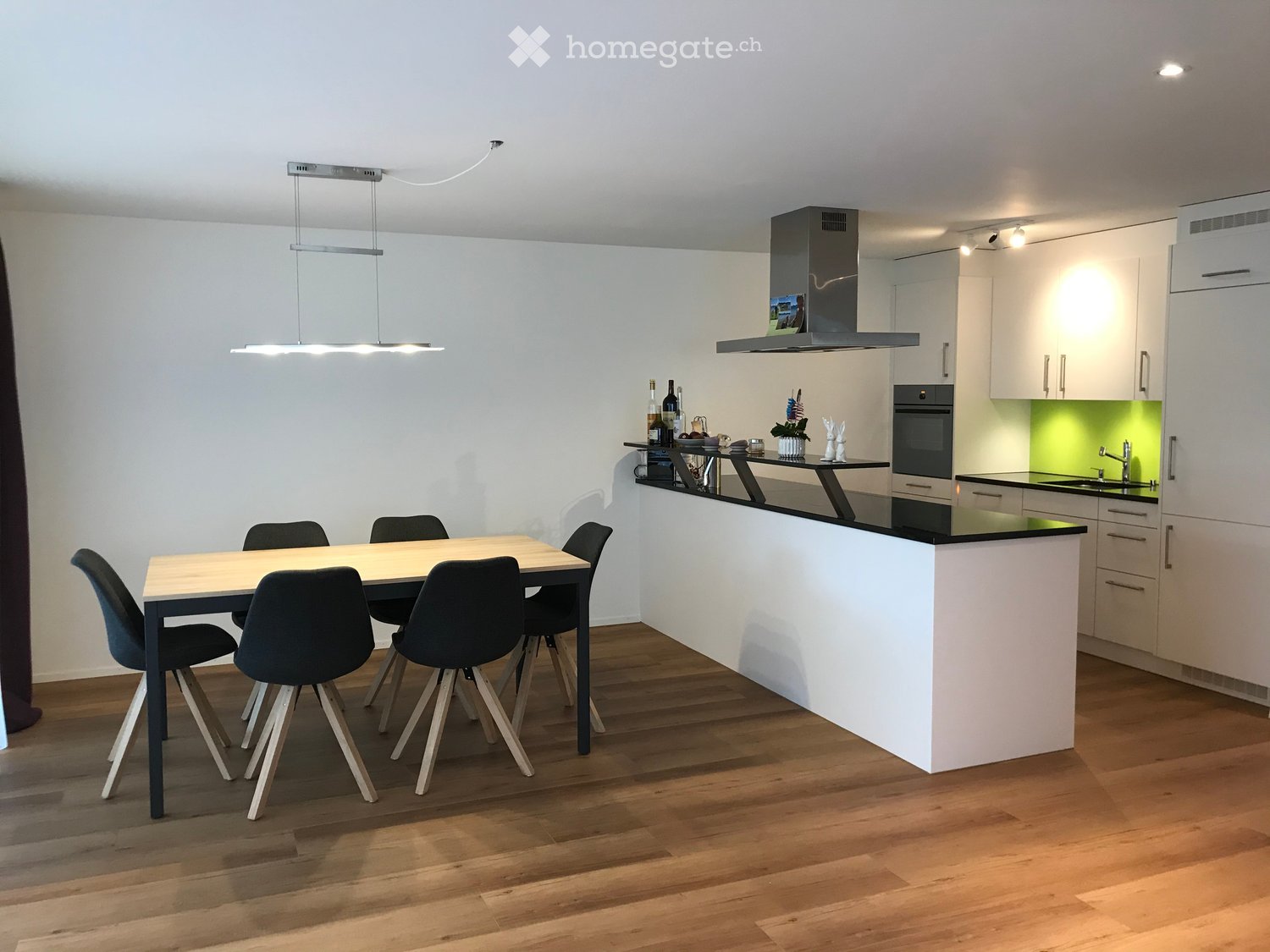 Modern kitchen with white cabinets, black countertops, a central island, a dining table with chairs, and a hanging light fixture.