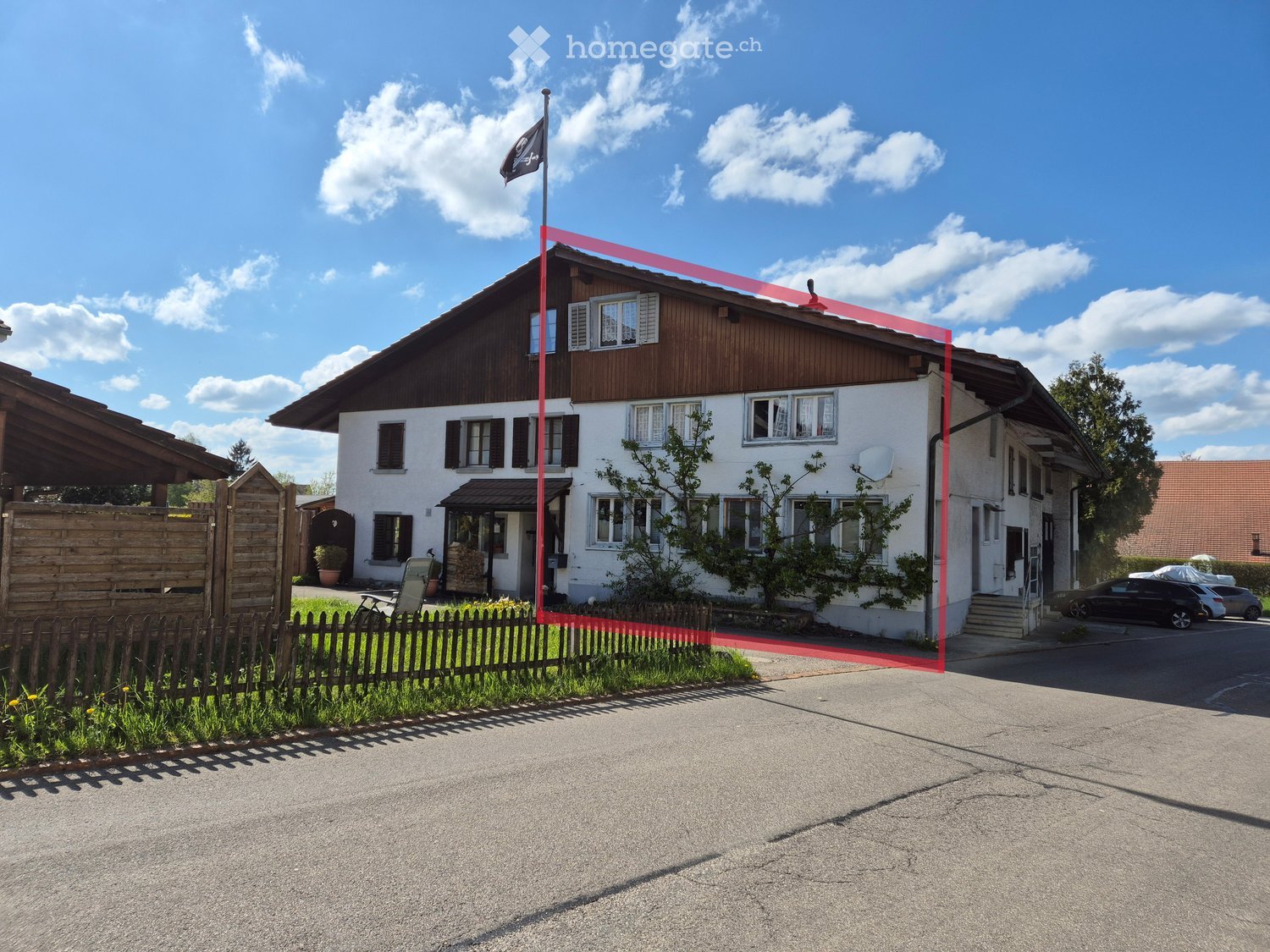 Two-story house with white walls, wooden roof, multiple windows, and a small garden area with a wooden fence.