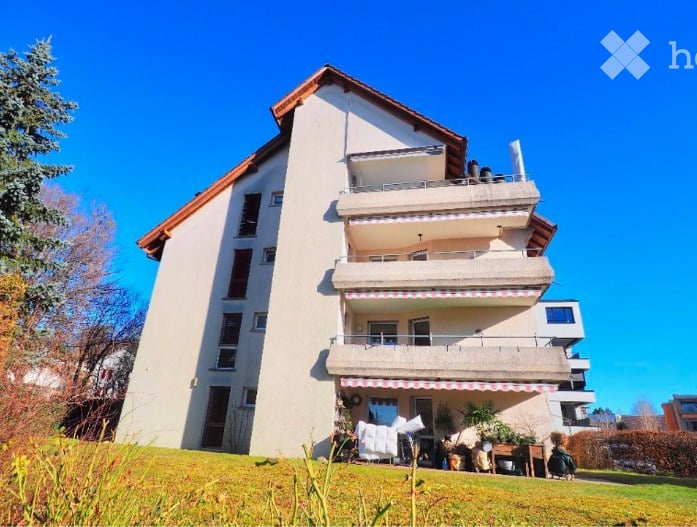 Modern multi-story residential building with balconies, large windows, and a well-maintained lawn in front.