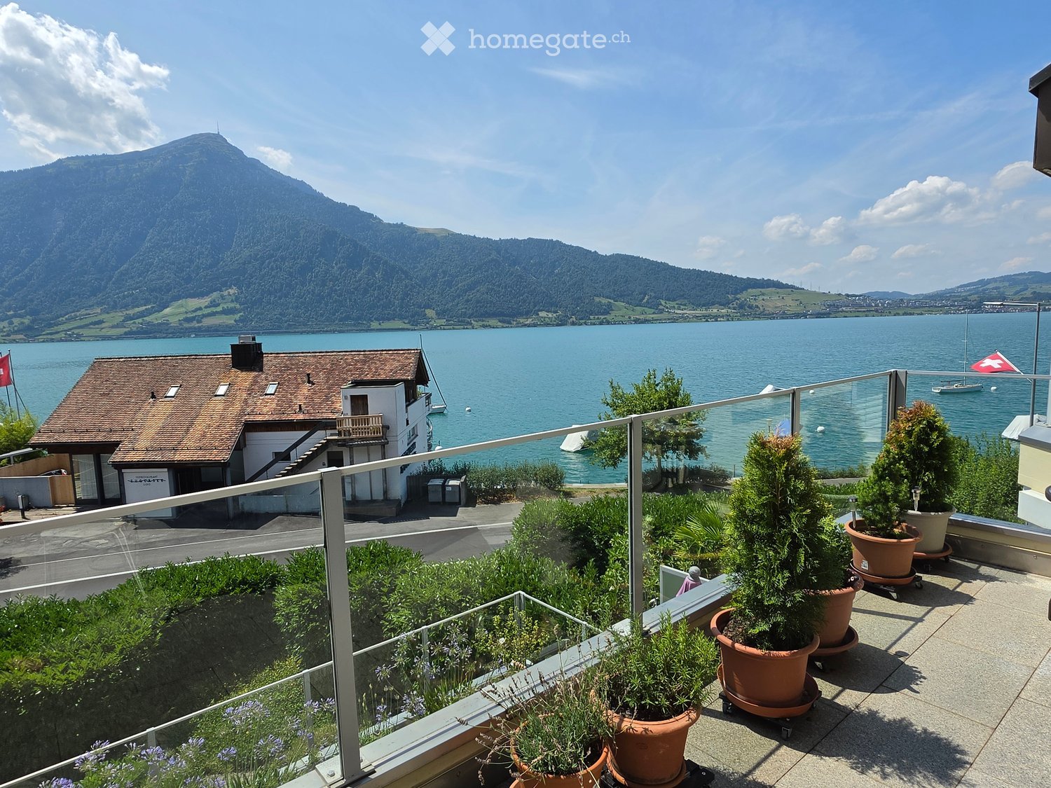 Balcony with glass railing, potted plants, and scenic view of a lake and mountains.
